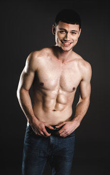 Portrait of cheerful young man with attractive body holding hands on belt. Happy bare-chested guy concept
