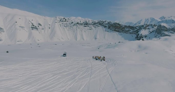 Aerial landing near a helicopter and a group of skiers and snowboarders in the winter mountains