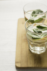 glass with water, apples and mint on a wooden board.