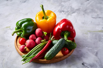Wooden plate with vegetables for a vegetarian salad on white textured background, close-up, selective focus