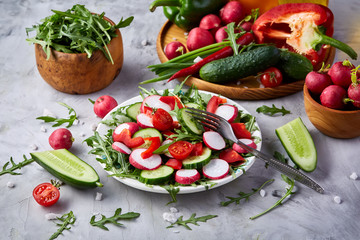 Creative fresh vegetable salad with ruccola, cucumber, tomatoes and raddish on white plate, selective focus