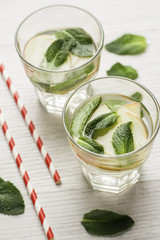 two glasses with water, apples and mint on a white background.