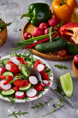 Creative fresh vegetable salad with ruccola, cucumber, tomatoes and raddish on white plate, selective focus