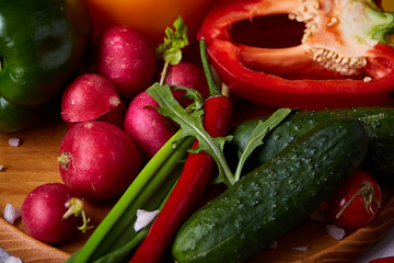 Wooden plate with vegetables for a vegetarian salad on white textured background, close-up, selective focus