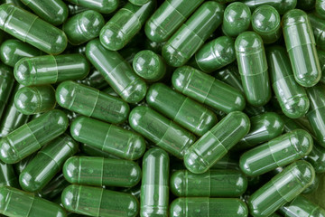 Green Spirulina powder, blue-green algae in clear capsules