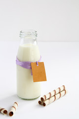 milk bottle with tag for writing wishes, next to her chocolate wafer tubes on white background