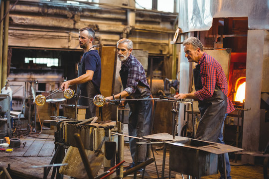 Team of glassblowers shaping a glass on the blowpipe