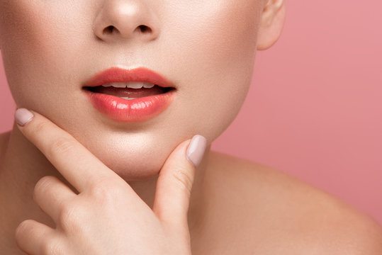 Close up of female lips painted with natural tone gloss. Woman touching chin with two fingers. Isolated on background