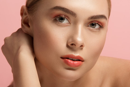 Close up of female face with soft derma and light makeup. She is looking at camera with tranquility. Isolated on rose background
