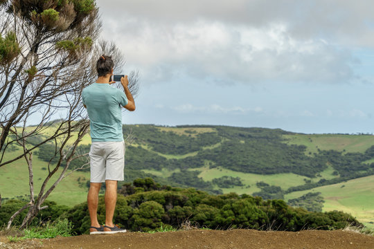 rear view of man taking photo of beautiful green valley with smartphone, New Zealand