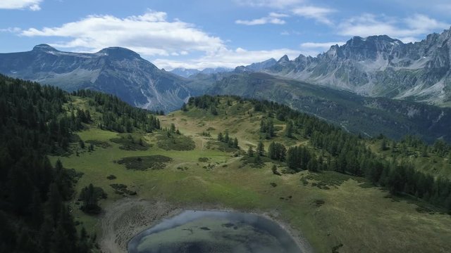 aerial forward over blue alpine lake revealing mountain forest valley in sunny summer with clouds.Europe Alps outdoors green nature scape mountains wild aerial establisher.4k drone establishing shot