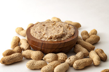 American breakfast, sweet food and snack high in calories concept with a bowl of crunchy peanut butter surrounded by peanuts still in shell, isolated on white background