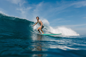 bearded young man in wet t-shirt riding waves on surfboard on sunny day