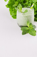 Healthy green spinach smoothies with leaf mint, greens, straw on white soft wood board, copy space.