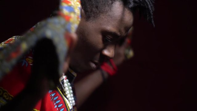 A man from Angola in traditional dashiki clothes puts a bright kerchief on his shoulders, bit slow motion