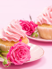 Cupcake with pink cream decoration and roses on pink pastel background.