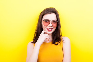 Sexy woman wearing sunglasses smiling to the camera on yellow background