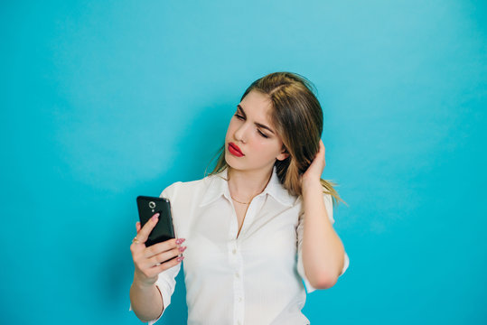 The girl is looking at the phone and smiling. Emotions of a person on a blue studio background. A girl communicates via video call in the phone