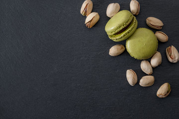 French dessert, sweet meringue based confectionery and expensive sweets concept with green pistachio flavored macaroon or macaron with a bunch of pistachios on black stone background with copy space