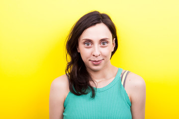 Face of real young woman looking to the camera on yellow background in studio