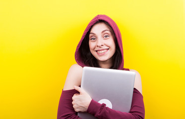 Smiling woman with a laptop in hands looking at the camera on yellow background in studio