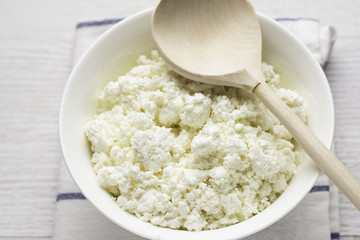 cup with cottage cheese, wooden spoon on white towel close-up.
