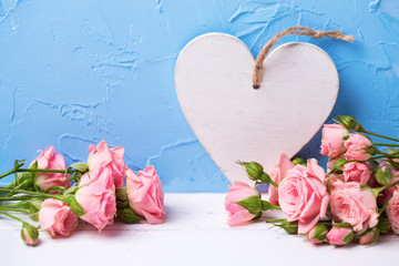 Frame from pink roses flowers and white heart on  light blue textured background.