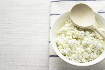 cup with cottage cheese, wooden spoon on a white towel.