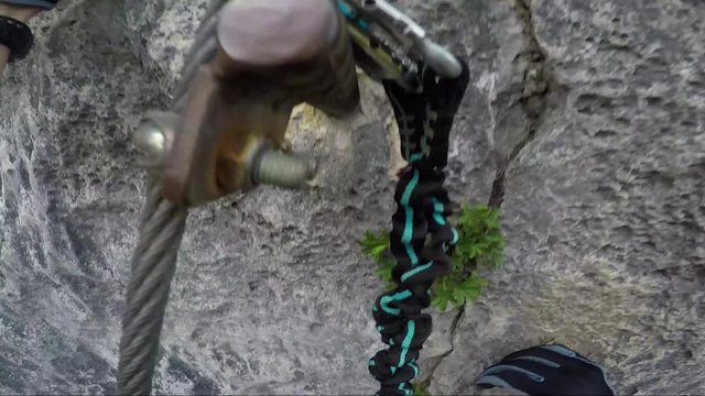 POV - a man readjusts his gloves and climbs up a cliff using iron pegs