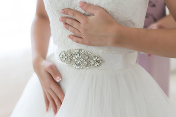 Bride holds her white lace wedding dress with ornamented belt