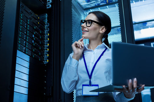 My good day. Alert beautiful woman working in a server cabinet and holding her laptop - Powered by Adobe