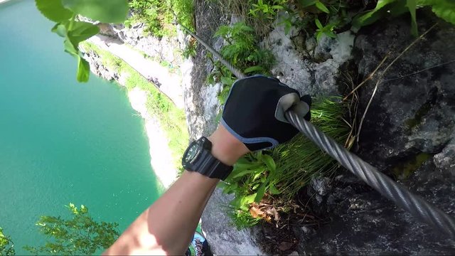 POV - a man climbs alongside a cliff above a river and rearranges the carabiners