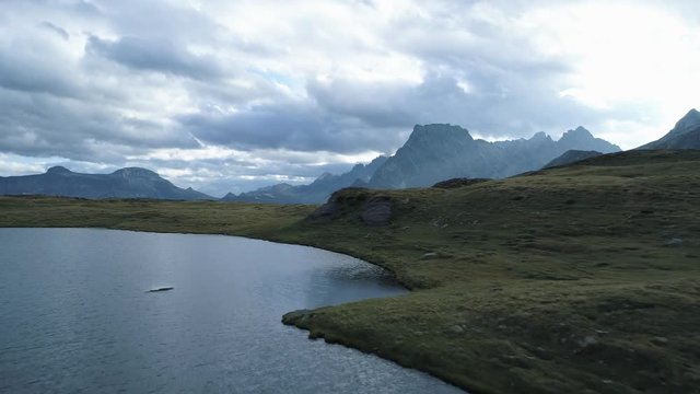 aerial forward above alpine lake revealing mountain valley in cloudy day dusk or dawn.Europe Italy Alps outdoors green nature scape mountains wild establisher.4k drone flight establishing shot