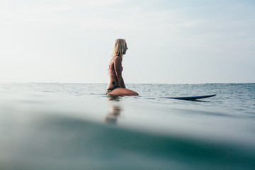 side view of young attractive woman sitting on surfboard in water