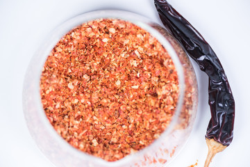Coarsely ground chilli peppers in glass bowl isolated on white background.