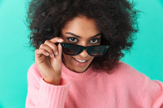 Fashion portrait of young woman 20s with shaggy hair smiling looking on camera in black modern sunglasses, isolated over blue background