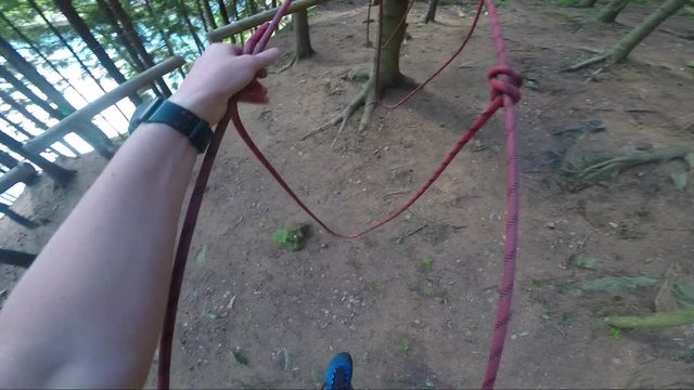 POV - a man walks across a rope obstacle in a forest