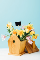 close up view of beautiful bouquet of flowers with blank chalkboard in birdhouse on wooden tabletop isolated on blue