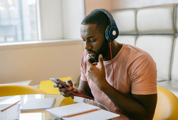 Portret of afro american man wearing headphones and holding a phone.