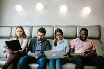 Group of students  read before exam, being focused in modern gadgets. Multiethnic business people work with digital devices.
