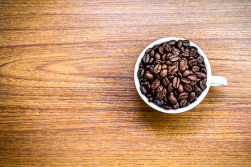 Coffee beans in white cup on wooden table.
