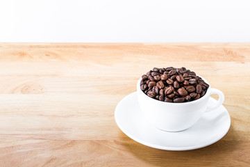 Coffee beans in white cup on wooden table.