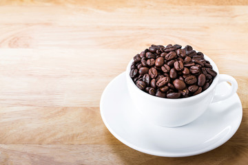 Coffee beans in white cup on wooden table.
