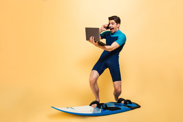 Excited young man on surfing board talking by phone using laptop computer.
