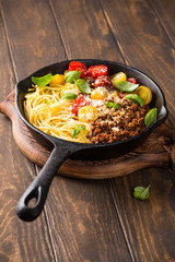 Healthy italian food. Delicious spaghetti Bolognaise or Bolognese with savory minced beef and cherry tomatoes garnished with parmesan cheese and basil in cost iron pan. Copy space.