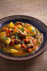 Stew, made with beef,  potatoes, carrots and green peas. Goulash soup in a bowl on wooden table. vertical
