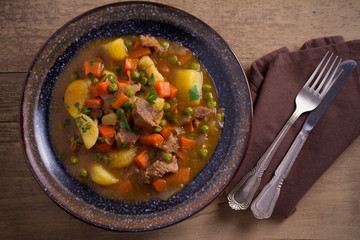 Stew, made with beef,  potatoes, carrots and green peas. Goulash soup in a bowl on wooden table. overhead, horizontal