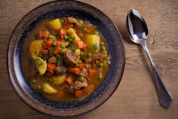 Stew, made with beef,  potatoes, carrots and green peas. Goulash soup in a bowl on wooden table. overhead, horizontal