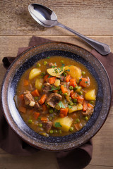 Stew, made with beef,  potatoes, carrots and green peas. Goulash soup in a bowl on wooden table. overhead, vertical