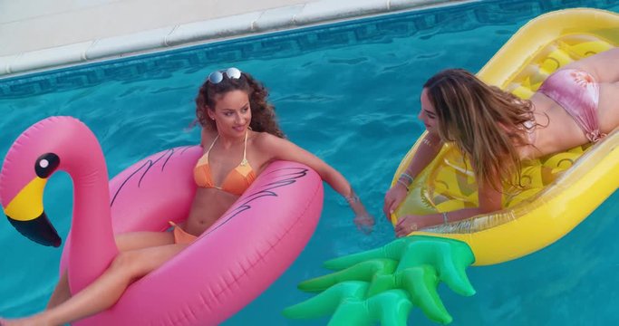 Young multi-ethnic female friends floating on summer inflatables in pool
